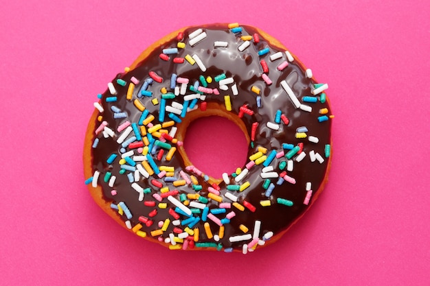 Brauner Schokoladenkrapfen mit bunten Streuseln auf einem rosa Hintergrund.