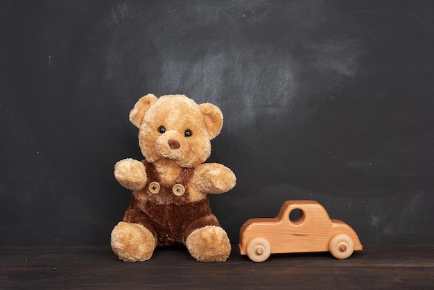 Foto brauner teddybär sitzt auf einem braunen holztisch und einem holzwagen hinter einer leeren schwarzen kreide