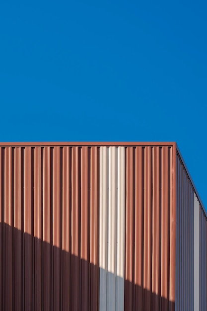 Brauner Wellstahl mit weißem Streifen an der Wand des Lagerhauses gegen den klaren blauen Himmel