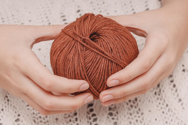 Brauner Wollknäuel in den Händen auf dem Hintergrund einer weißen gestrickten Tischdecke