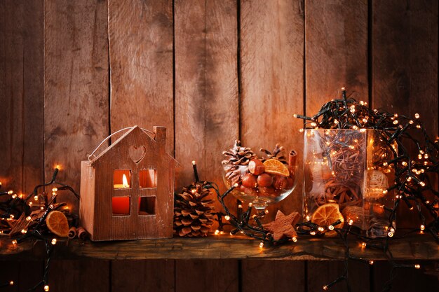 Braunes Haus mit Kerze und elektrischer Girlande auf Holz