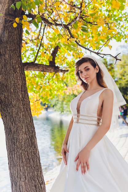 Braut, die in einem grünen Parkmädchen in einem weißen Kleid auf einem Hintergrund des Grüns aufwirft.