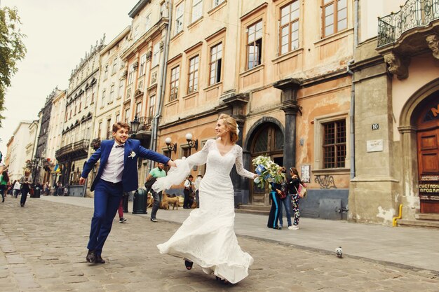 Braut hält die Hand des Bräutigams fest, die mit ihm entlang alter europäischer Straße läuft