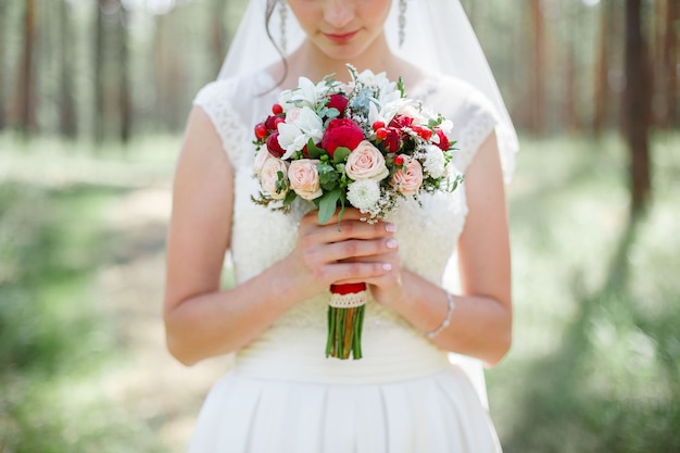 Braut hält Hochzeitsstrauß der weißen und roten Blumen im Freien junges Mädchen im weißen Kleid mit Blumen