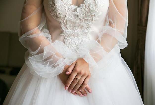 Braut hält ihre Hände auf Taille Schönes langärmliges Kleid Spitzenstoff Details zum Hochzeitsmorgen