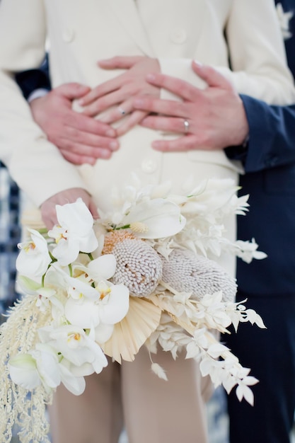 Braut im beigen Hochzeitsanzug Händchen haltend mit Bräutigam im dunkelblauen Anzug Stilvolles Hochzeitskonzept