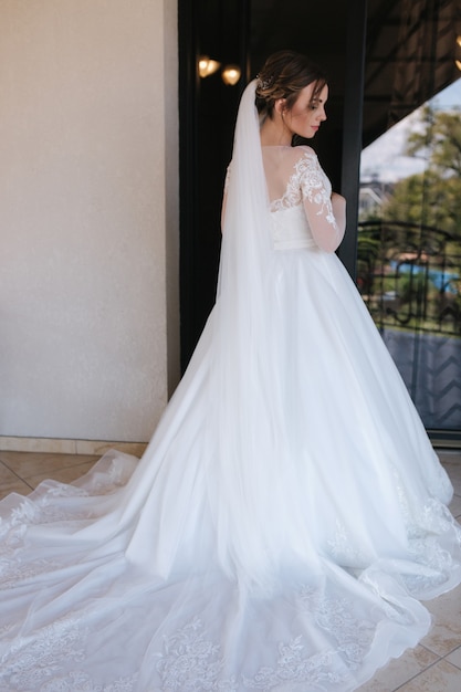 Braut im Hochzeitskleid stehen auf Balkon in der Nähe des Fensters