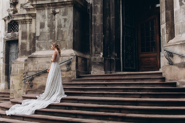 Braut im Kleid mit langer Schleppe steht vor einer alten gotischen Kirche