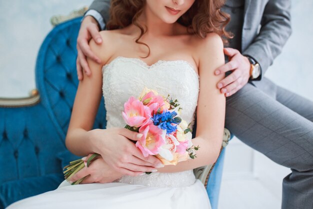 Braut im schönen Kleid und im Bräutigam in der grauen Klage, die zuhause auf Sofa sitzt