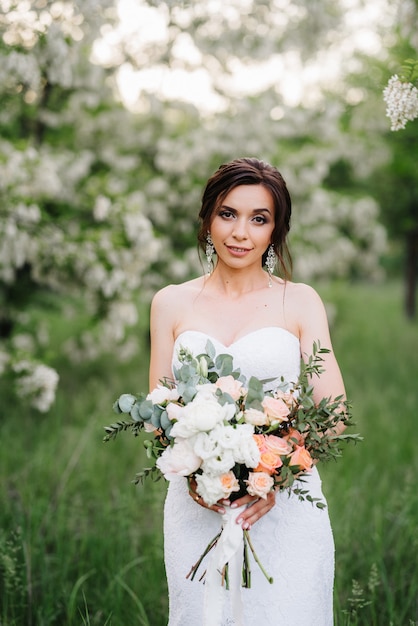 Braut im weißen Kleid mit großem Frühlingsstrauß in einem grünen Wald