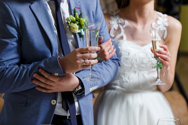 Braut im weißen Kleid und Bräutigam im blauen Anzug halten in ihren Händen Champagnergläser