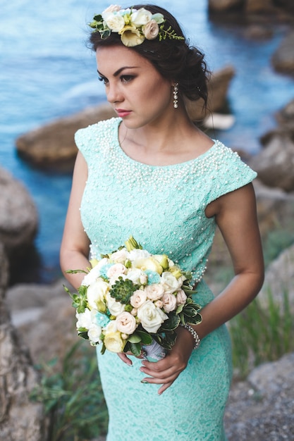 Braut in der Natur in den Bergen in der Nähe des Wassers. Kleiderfarbe Tiffany. Braut posiert mit Blumenstrauß.