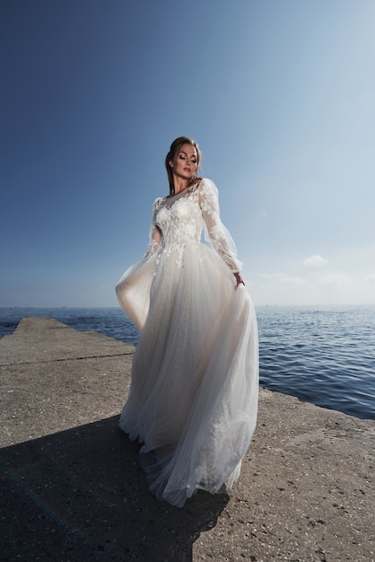 Braut in einem Hochzeitskleid am Strand am Meer gegen den blauen Himmel