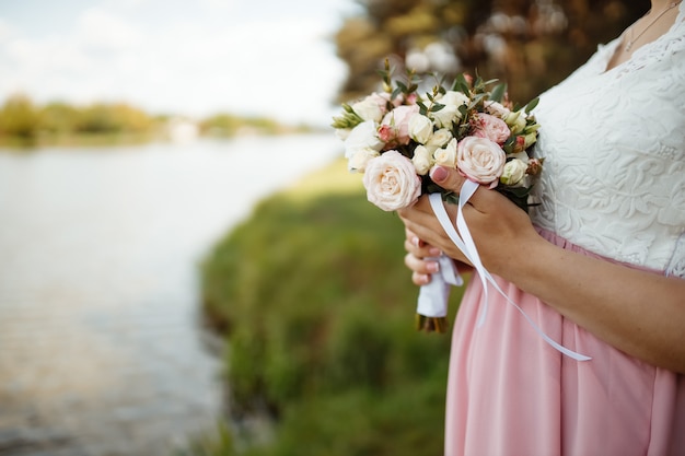 Braut in einem schönen kleid mit einem zug, der einen blumenstrauß und grün hält