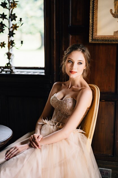 Braut in einem schönen Kleid sitzt auf einem Stuhl an einem Tisch in einem alten Gebäude