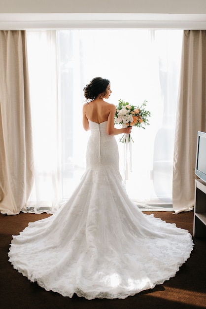 Braut in einem weißen Kleid mit Blumenstrauß in einem Hotelzimmer