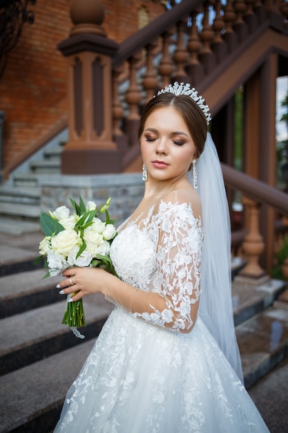 Braut in einem weißen Kleid mit einem Blumenstrauß in den Händen und einer Krone auf dem Kopf