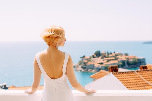 Braut in einem weißen Kleid steht seitlich und schaut auf die Insel Sveti Stefan in der Nähe von Budva Montenegro