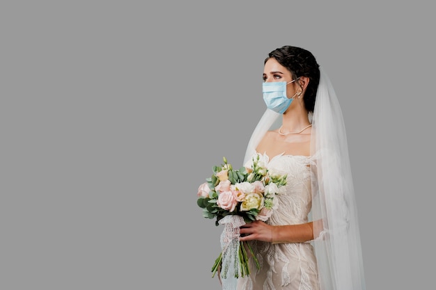 Braut in medizinischer Maske und Hochzeitsstrauß in der Quarantänezeit von Coronavirus covid-19. Attraktives Mädchen im Studio.
