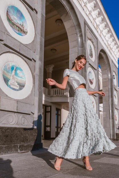 Braut in sanft türkisfarbenem Taftkleid tanzt auf der Veranda des Gebäudes mit originaler Architektur