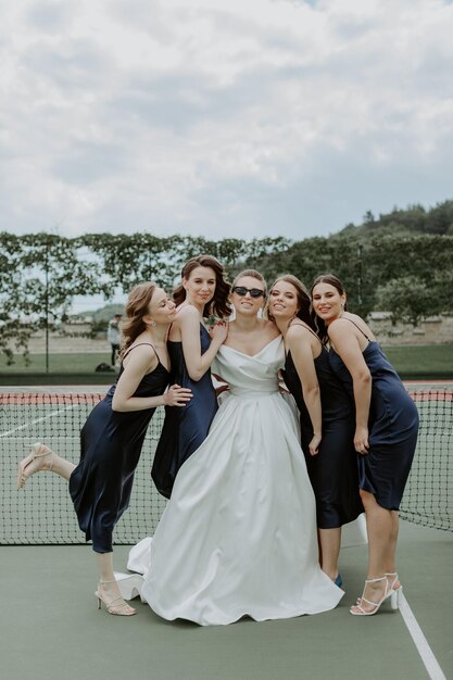 Braut mit den Brautjungfern in den glänzenden Kleidern auf dem Tennisplatz