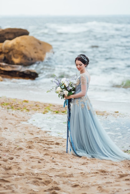 Braut mit einem Blumenstrauß am Strand in der Nähe des Wassers