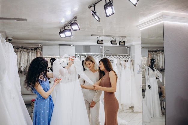 Braut mit Freunden, die Hochzeitskleid in Boutique auswählen