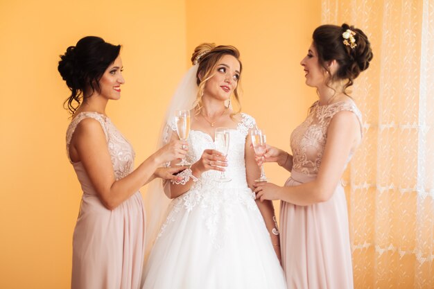 Braut mit fröhlichen Freundinnen bei der Hochzeit trinken Champagner aus Gläsern