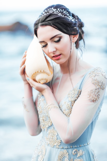 Braut mit großer Muschel am Strand im blauen Brautkleid