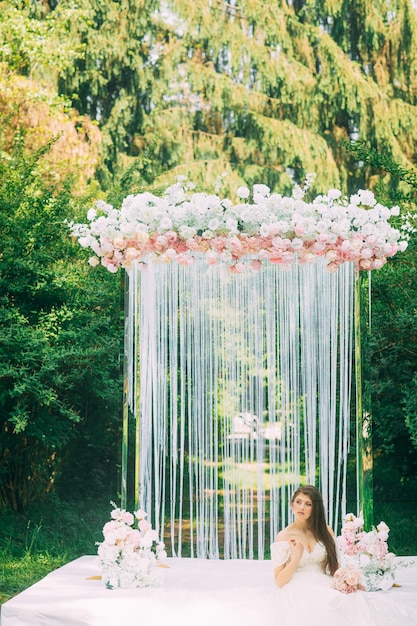 Braut nahe Hochzeitsbogen mit Blumen