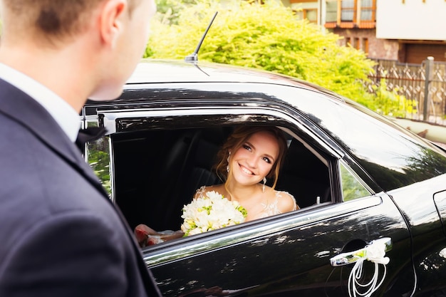 Braut sitzt in einem schwarzen Auto und sieht ihren Verlobten durch ein Fenster an