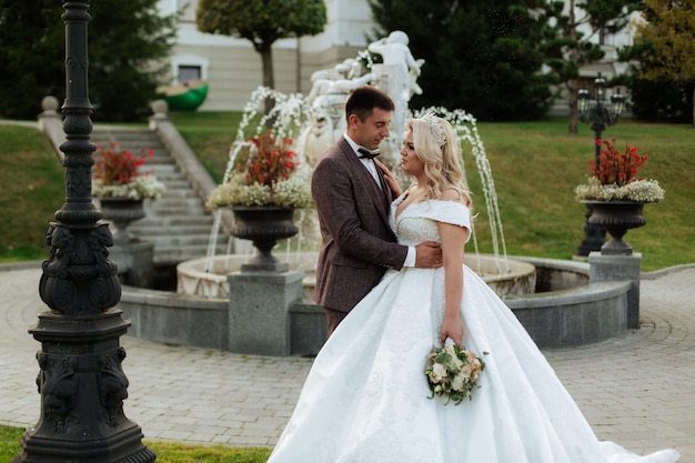 Braut und Bräutigam am Hochzeitstag, der draußen auf Frühlingsnatur geht. Brautpaar, glückliche frisch verheiratete Frau und Mann, die im grünen Park umarmen. Liebevolles Hochzeitspaar im Freien.