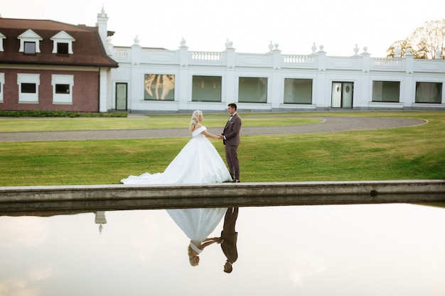 Foto braut und bräutigam am hochzeitstag, der draußen auf frühlingsnatur geht. brautpaar, glückliche frisch verheiratete frau und mann, die im grünen park umarmen. liebevolles hochzeitspaar im freien.