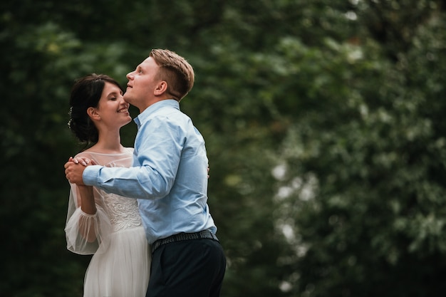 Braut und Bräutigam am Hochzeitstag draußen gehend auf Frühlingsnatur. Brautpaar, glückliche Jungvermähltenfrau und Mann, die im grünen Park umfassen. Liebevolle Hochzeitspaare im Freien. Braut und Bräutigam