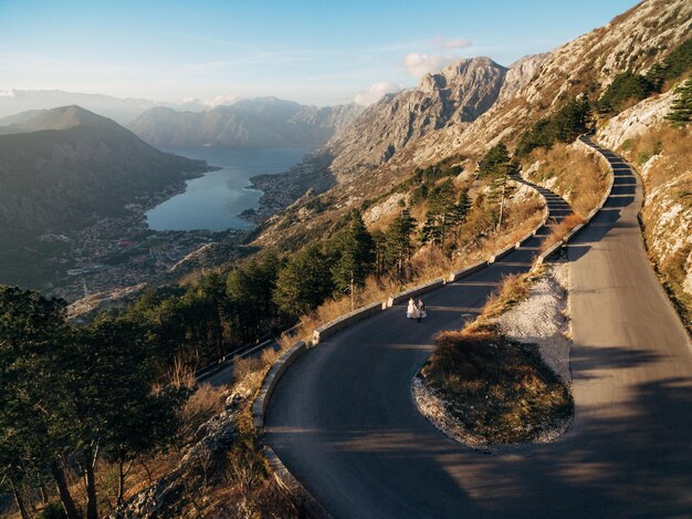 Braut und Bräutigam gehen auf einer hochgebirgigen Asphaltstraße über die Bucht