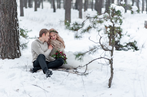 Braut und Bräutigam in beigen Strickpullovern im verschneiten Wald. Jungvermählten berühren die Stirn. Winterhochzeit. Speicherplatz kopieren