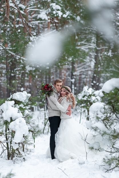 Braut und Bräutigam in beigen Strickpullovern im verschneiten Wald. Jungvermählten berühren die Stirn. Winterhochzeit. Speicherplatz kopieren