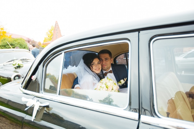 Braut und Bräutigam in einem Oldtimer. Sie sind glücklich.