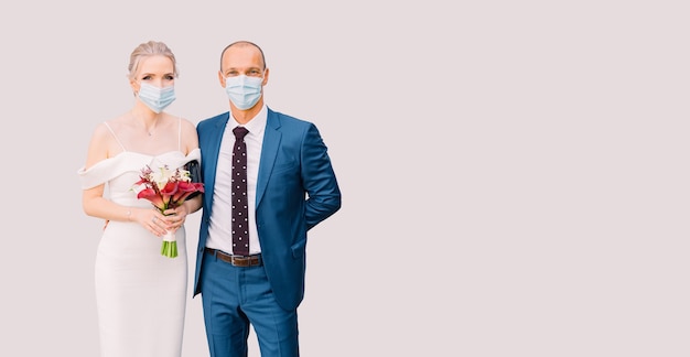 Braut und Bräutigam in medizinischen Masken auf einem isolierten Hintergrund. Hochzeit für zwei während der Isolation, Covid