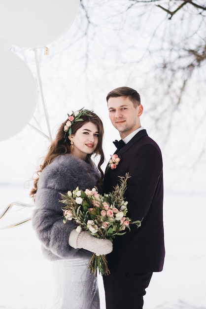 Braut und Bräutigam inmitten einer verschneiten Landschaft mit großen weißen Luftballons