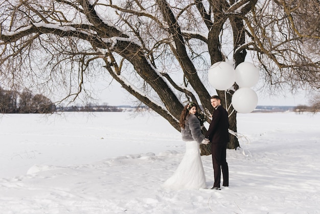 Braut und Bräutigam inmitten einer verschneiten Landschaft mit großen weißen Luftballons