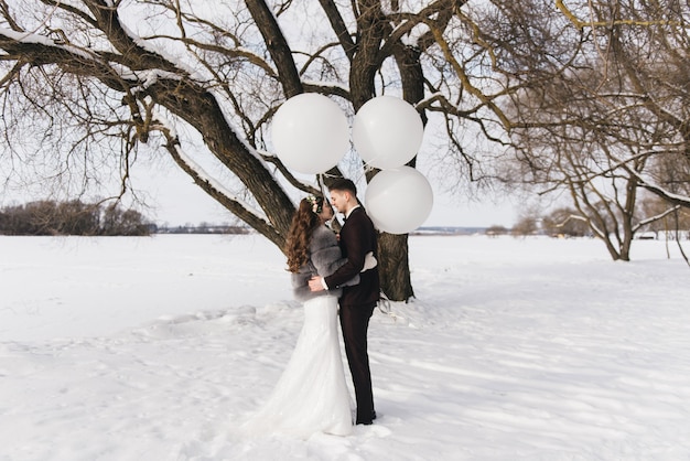 Braut und Bräutigam inmitten einer verschneiten Landschaft mit großen weißen Luftballons