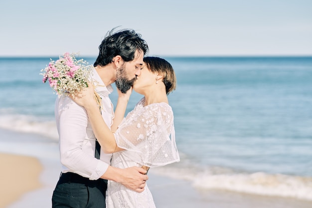 Braut und Bräutigam küssen sich am Strand und feiern glücklich ihre Hochzeit