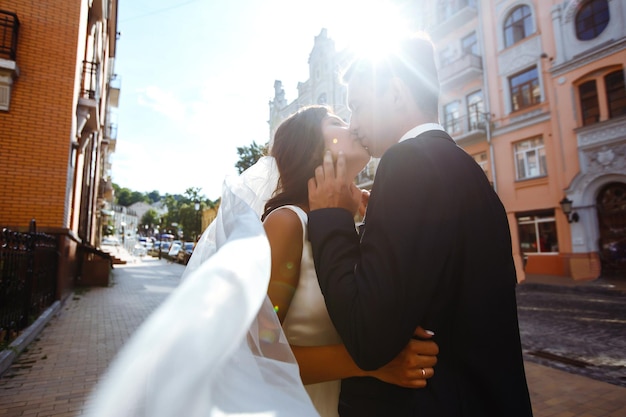 Braut und Bräutigam küssen sich zärtlich im Schatten eines fliegenden Schleiers. Gemeinsame Hochzeitsliebe