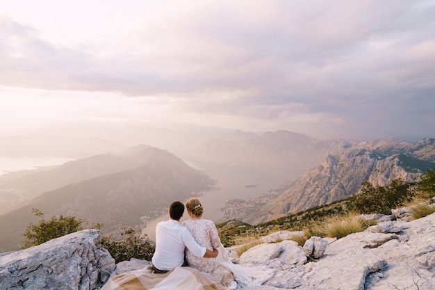 Braut und Bräutigam sitzen auf dem Berg und schauen auf die Bucht