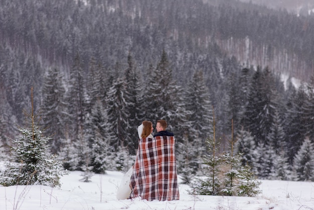 Braut und Bräutigam stehen vor dem Hintergrund der Berge und kuscheln sich unter einen Teppich, um sich warm zu halten. Winterhochzeit