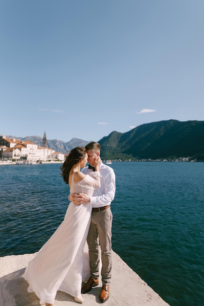 Braut und Bräutigam umarmen sich mit ihrer Stirn, die sich auf dem Pier in Montenegro berühren.