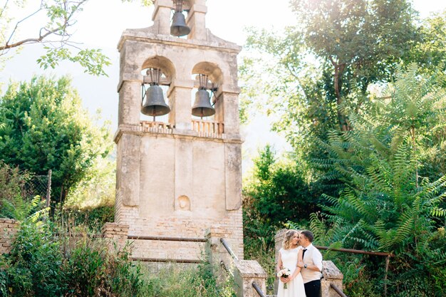 Braut und bräutigam umarmen und küssen sich am alten glockenturm in der nähe der kirche in prcanj