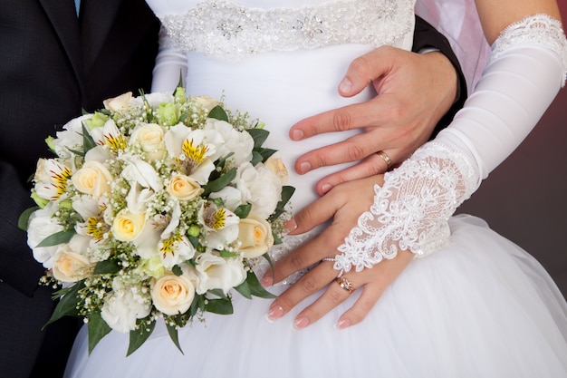 Braut- und Bräutigamhände mit Eheringen und Blumenstrauß von Rosen