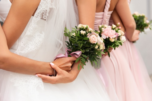 Braut und Brautjungfern in rosa Kleidern, die mit Blumensträußen am Hochzeitstag aufwerfen